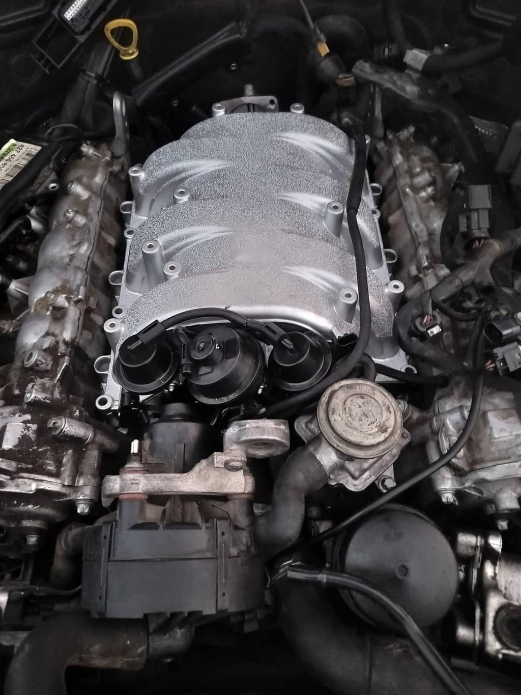 Engine bay close-up of installed silver intake manifold with black vacuum lines