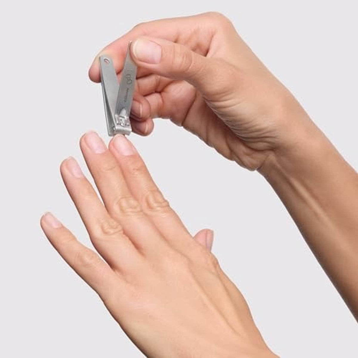 Hand holding a nail clipper trimming fingernails