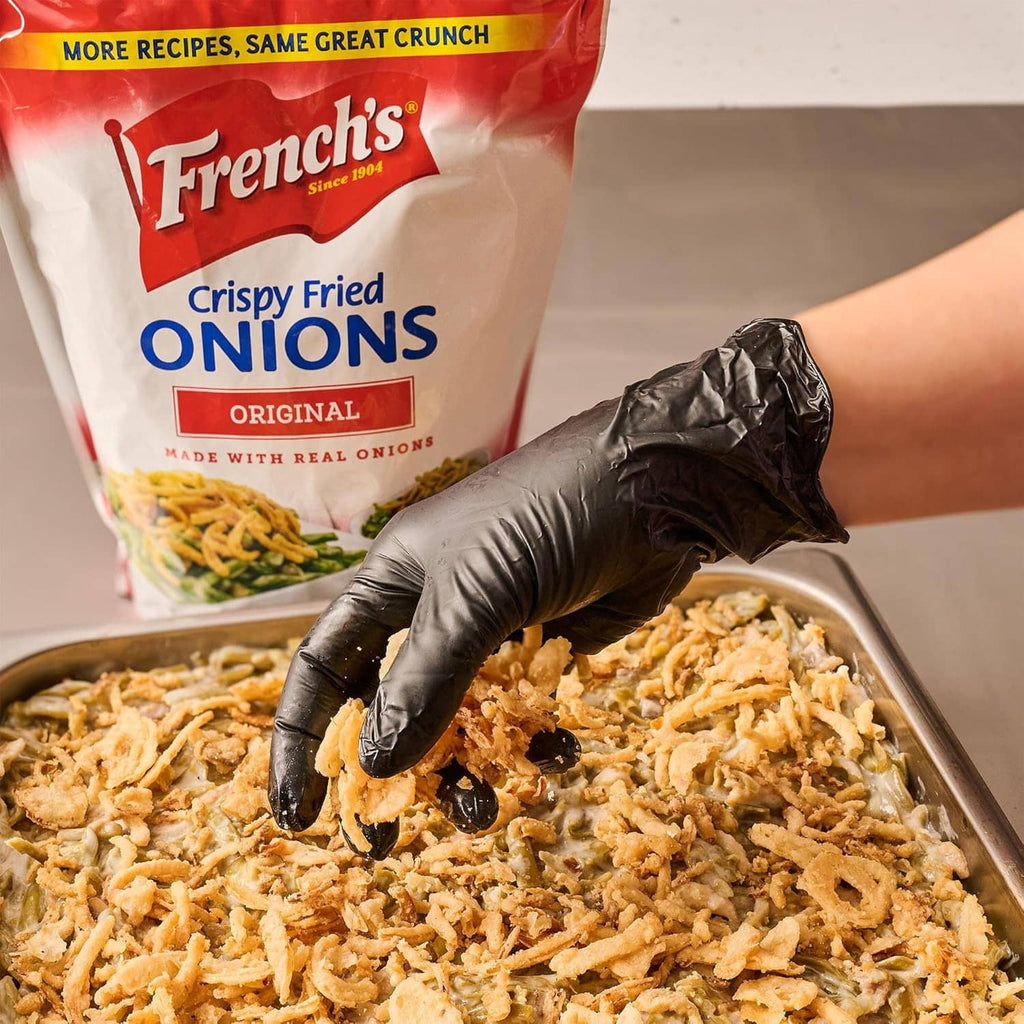 Hand in a glove sprinkling crispy fried onions from a pouch onto a metal tray