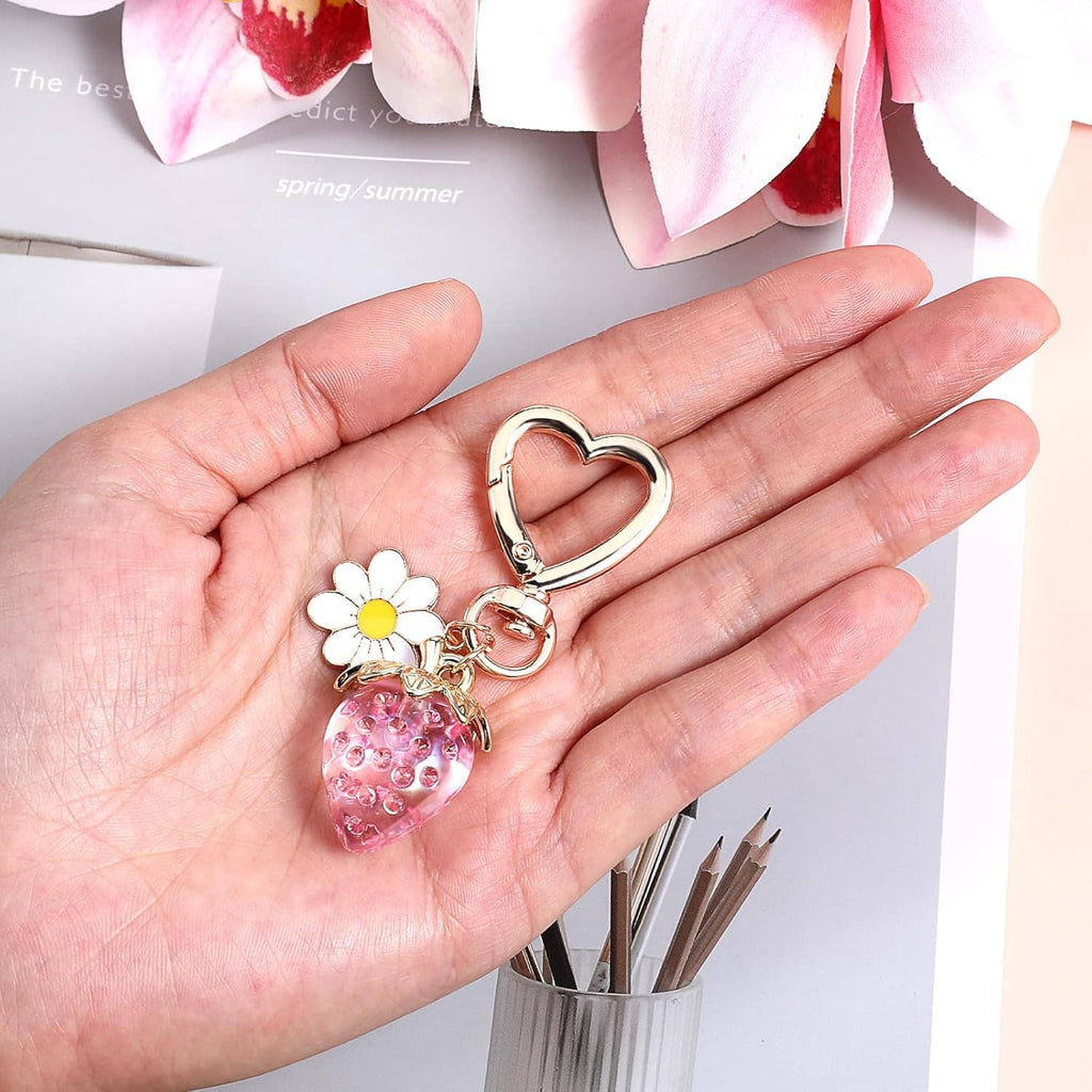 Heart keychain with strawberry charm and daisy flower, shown held in a hand