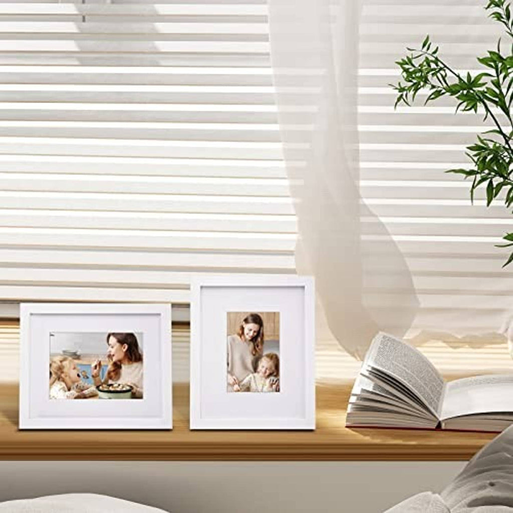 White picture frames with plexiglass displaying photos on tabletop near plants
