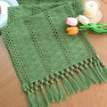 Green woven table runner with fringe tassels and textured diamond stitch.