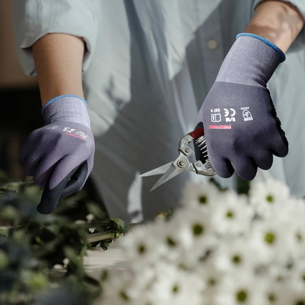 Gray knit gloves with black nitrile dotted palms holding flowers outdoors