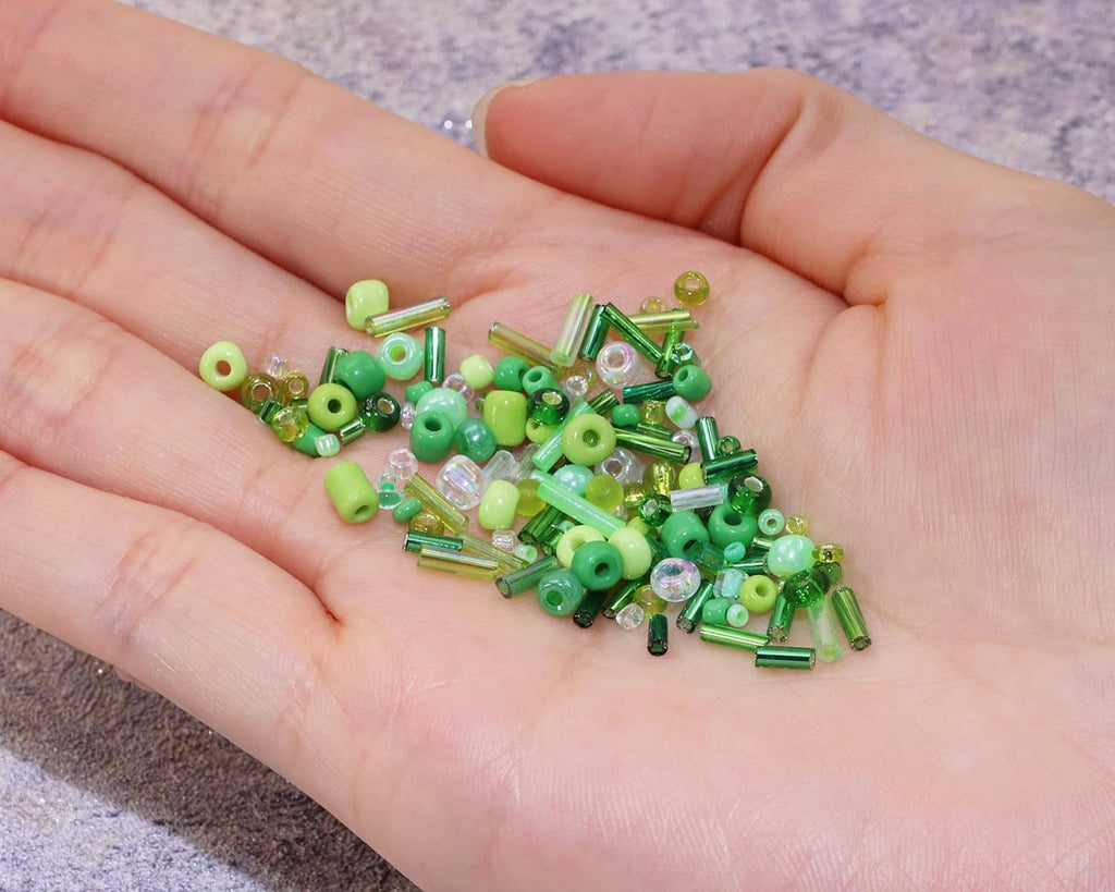 Assorted green seed beads and bugle tubes in an open palm