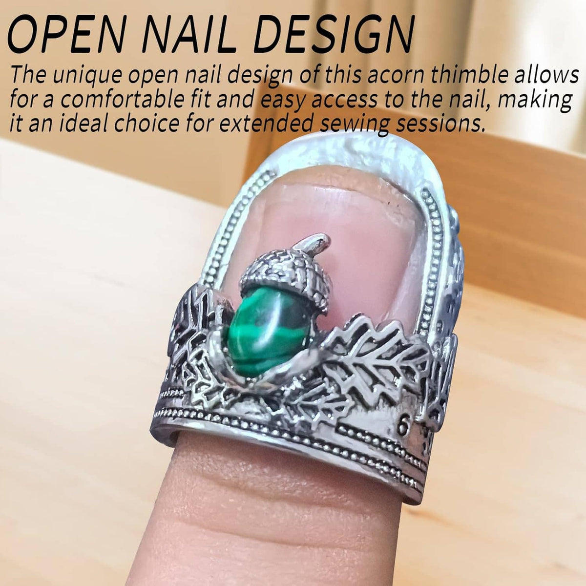 Open nail thimble worn on finger; silver metal with green acorn charm, engraved edge