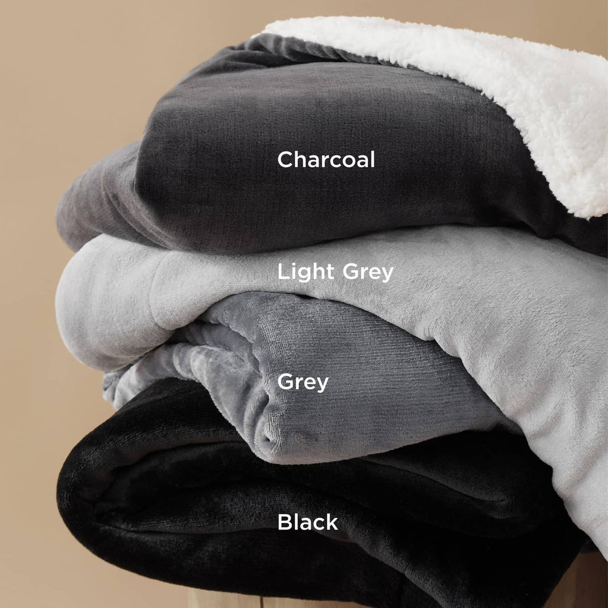 Stacked sherpa fleece throw blankets in charcoal, light grey, grey, and black