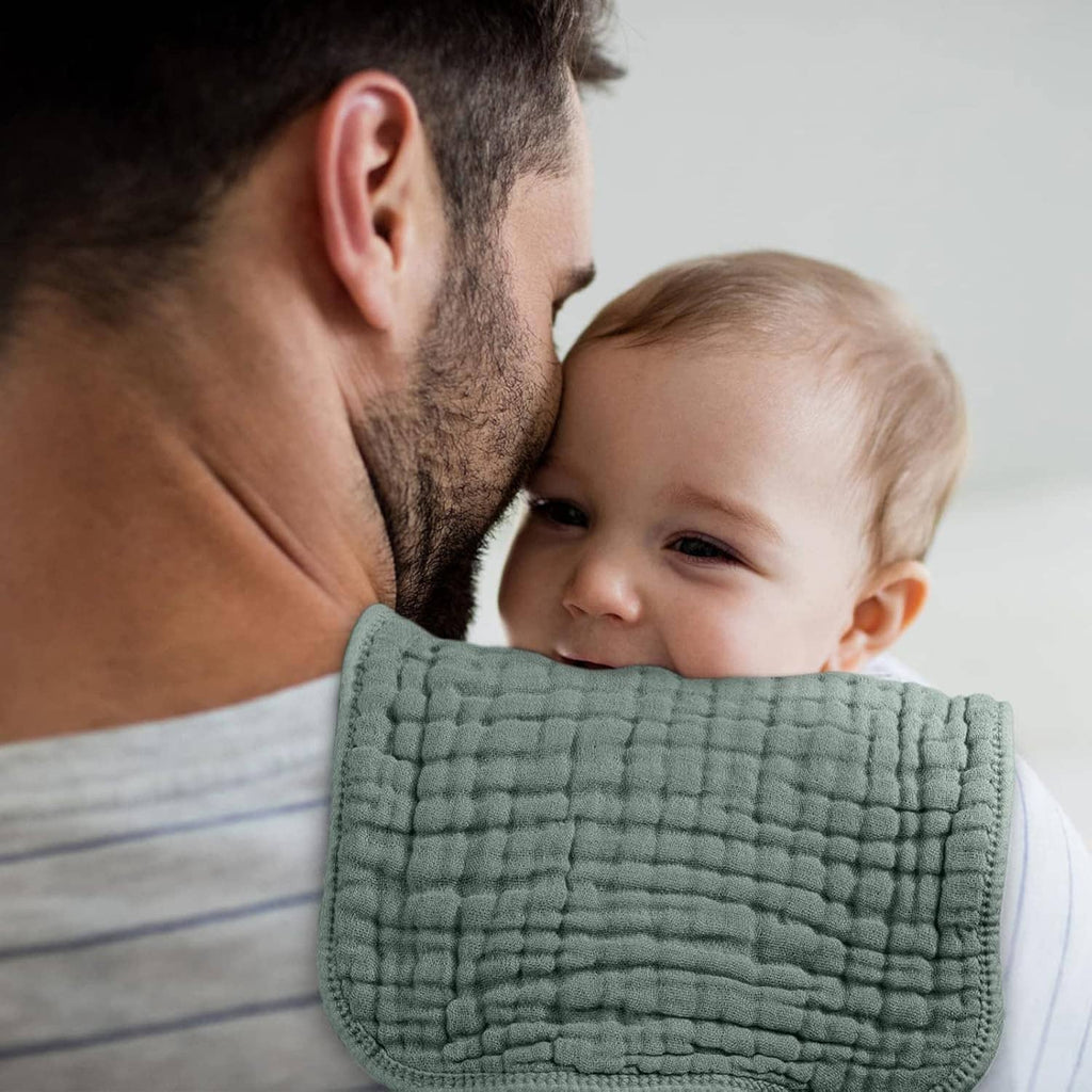 Sage green muslin burp cloth held against baby’s chest while parent supports them