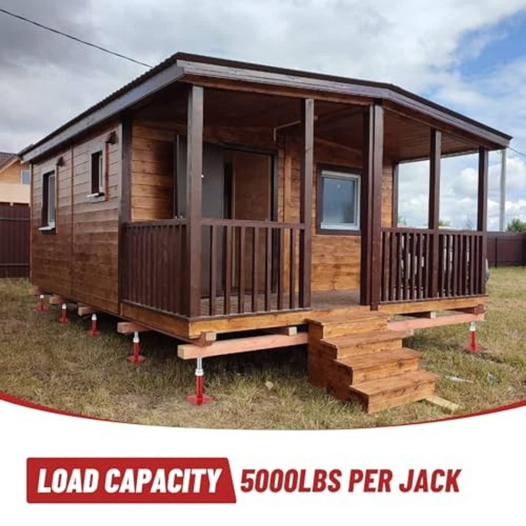Red floor jack stands holding up a wooden home frame on a ground platform