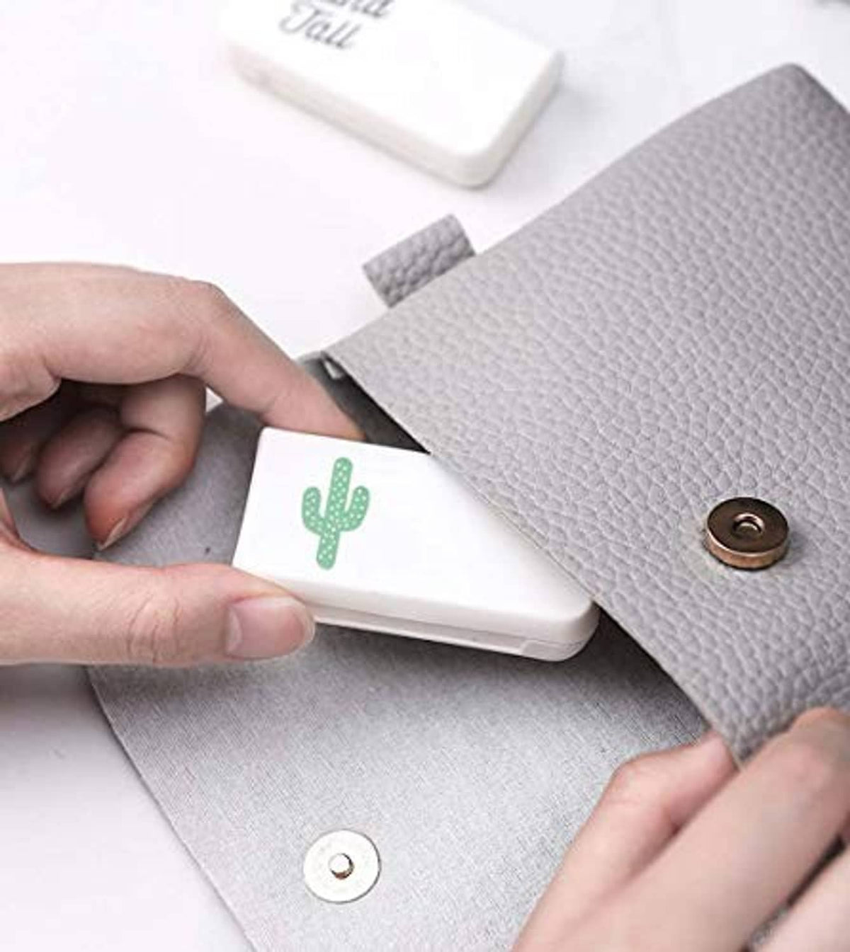 Small white pill organizer with cactus icon, hinged lid and slots visible in hands