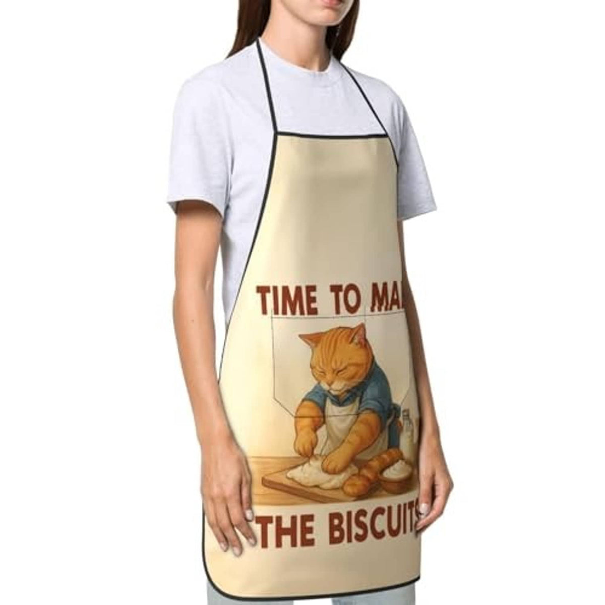 Beige chef bib apron on model over gray shirt; cat baking and biscuits graphic