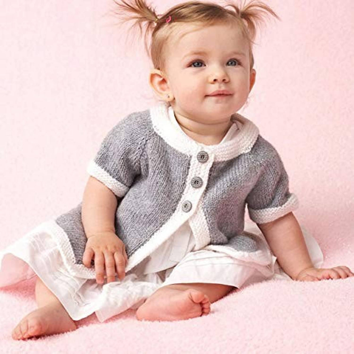 Light gray knitted baby cardigan over white romper, button front