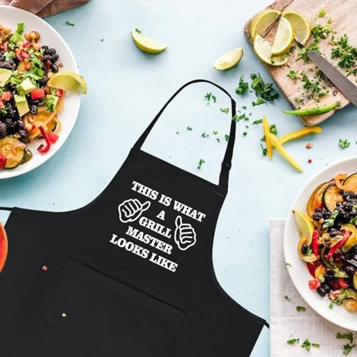 Black grilling apron with “Grill Master looks like” white graphic, flat lay on table