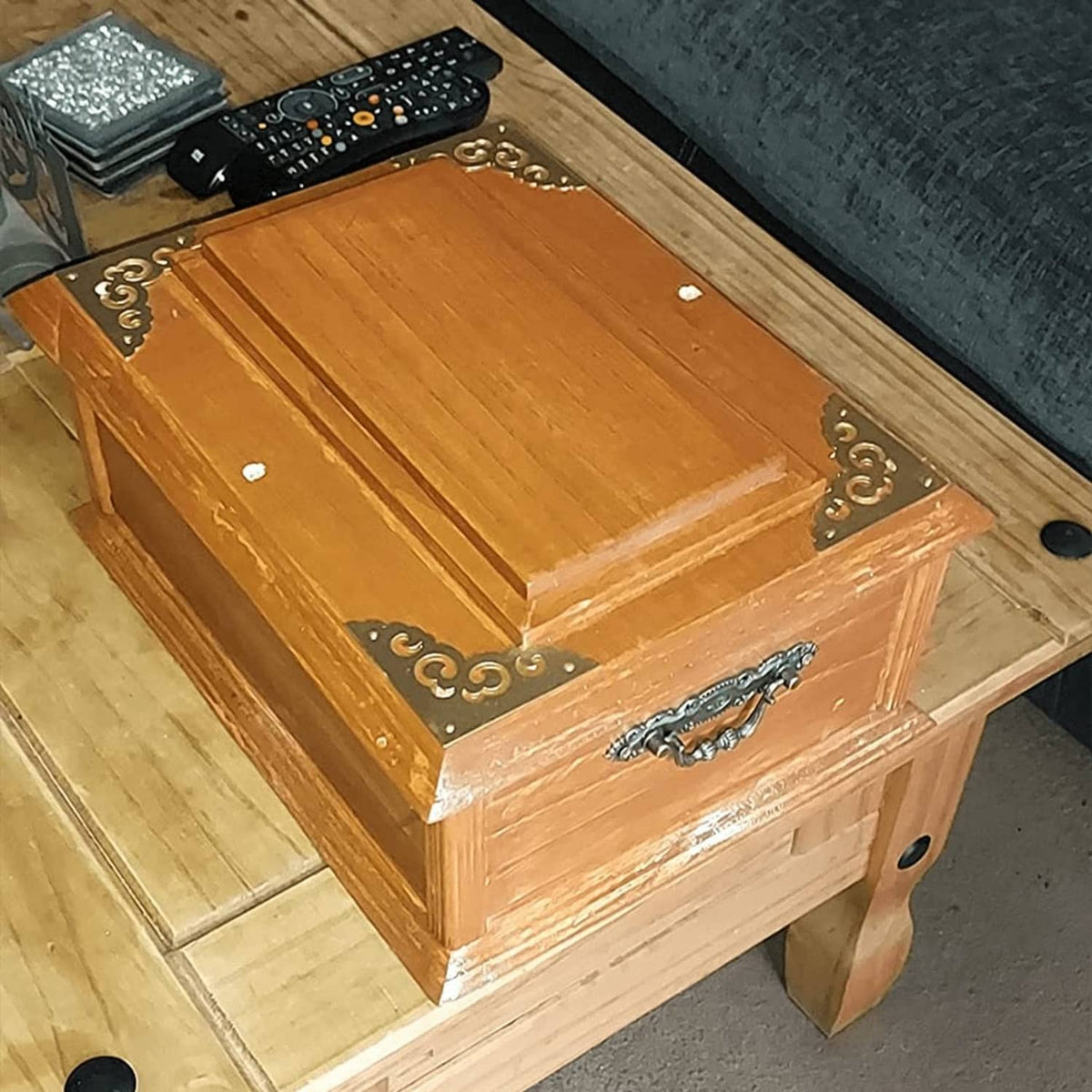 Brass corner bracket covers with ornate scroll cutouts installed on a wooden box table