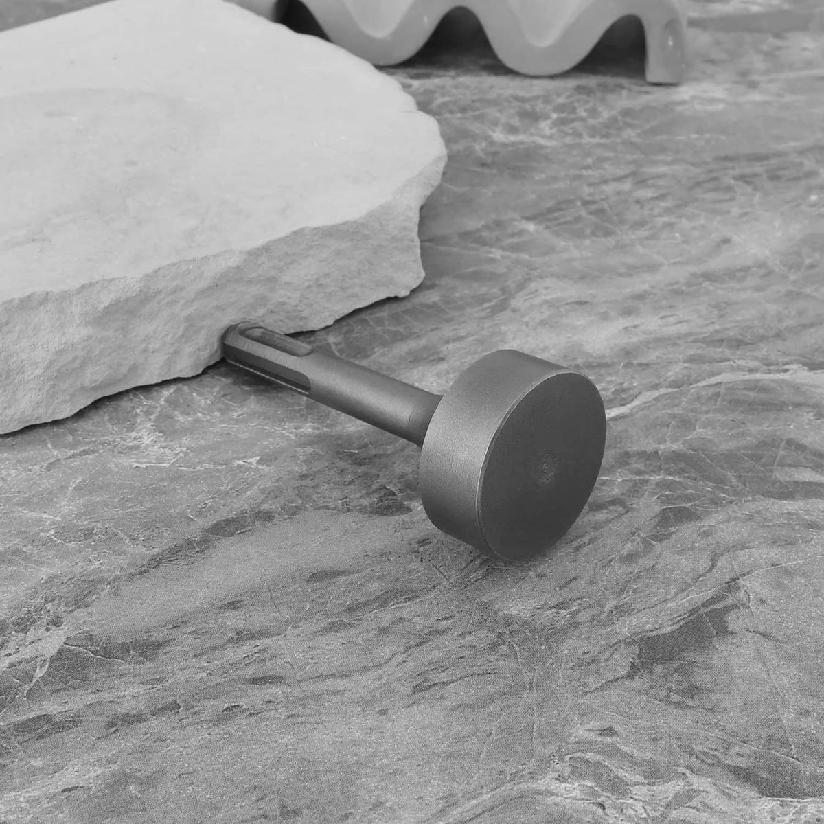 Grey ground rod driver adapter lying on stone near rock block