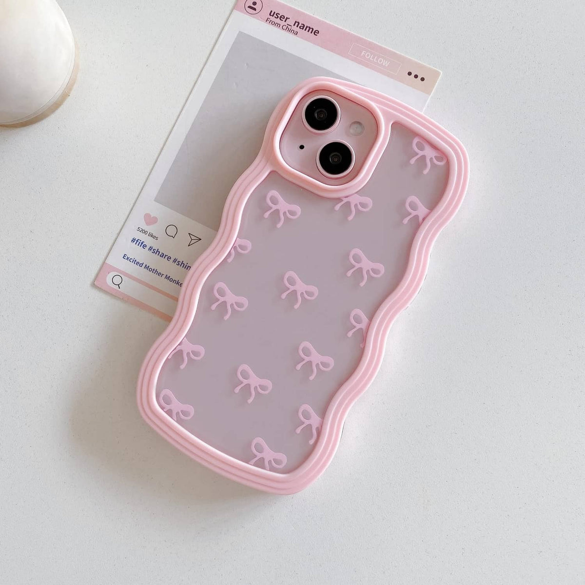 Pink clear iPhone case with repeating bow pattern and dual camera holes.