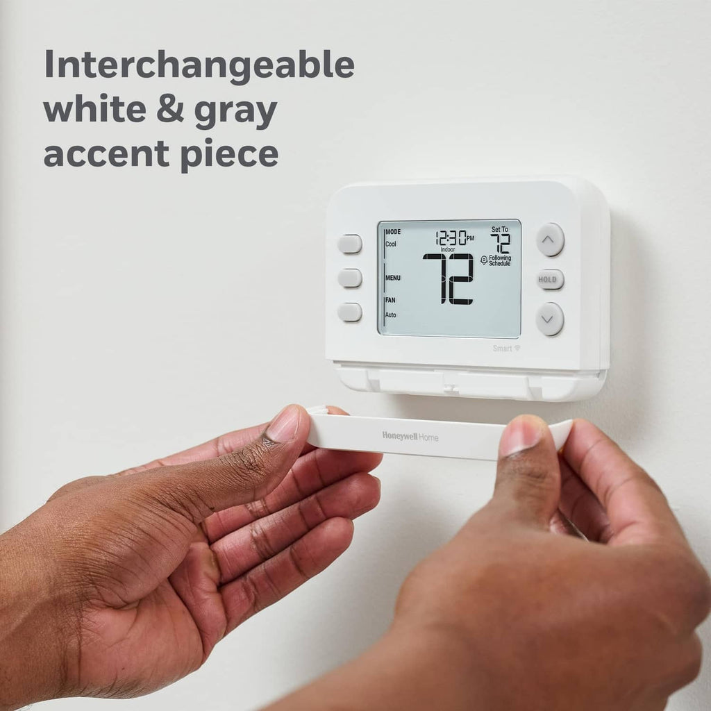 White and grey smart thermostat with LCD display, hands installing on a wall