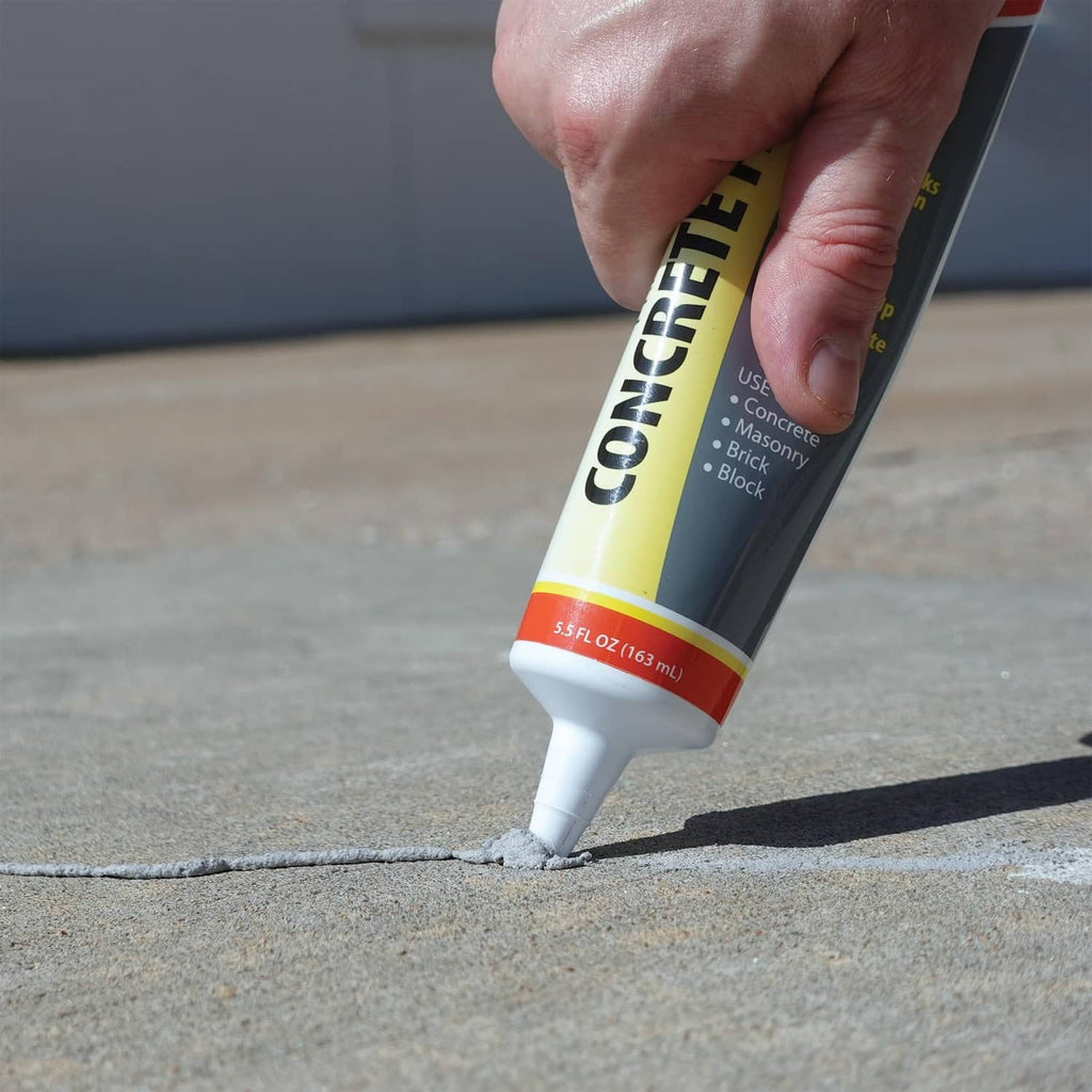 Concrete patch tube nozzle dispensing gray filler onto a concrete crack