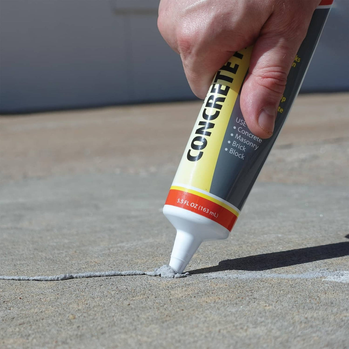 Concrete patch tube nozzle dispensing gray filler onto a concrete crack