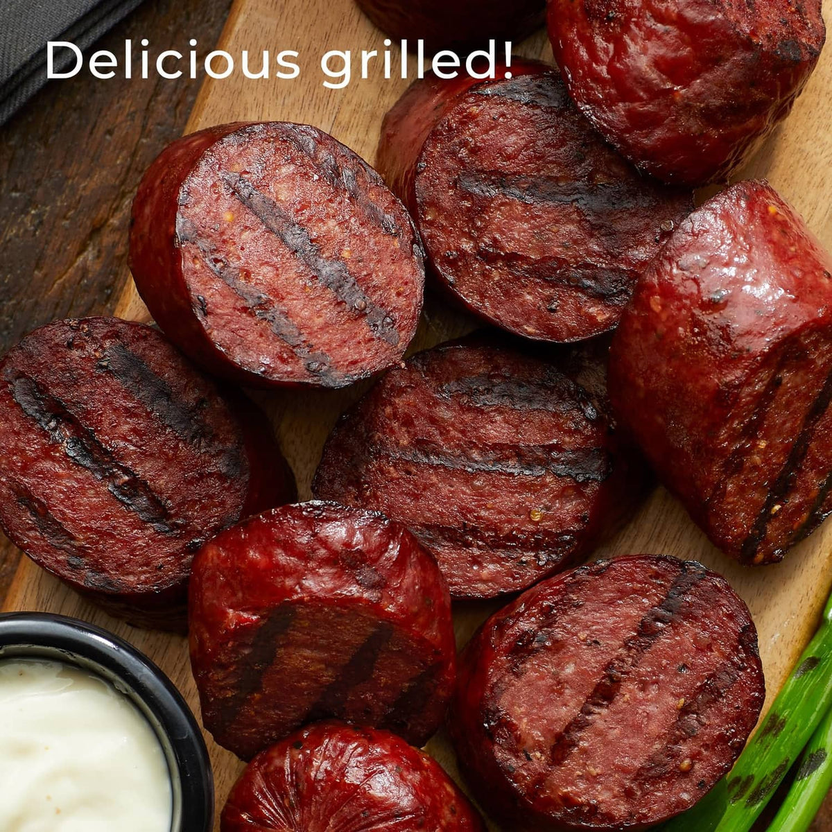 Grilled Beef Summer Sausage slices on a wooden board with a side of creamy dip