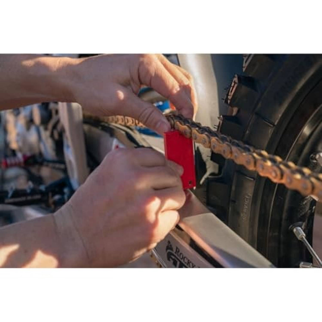 Hands using a red chain slack measuring tool on the rear wheel chain