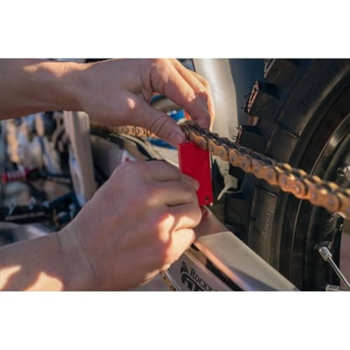 Hands using a red chain slack measuring tool on the rear wheel chain