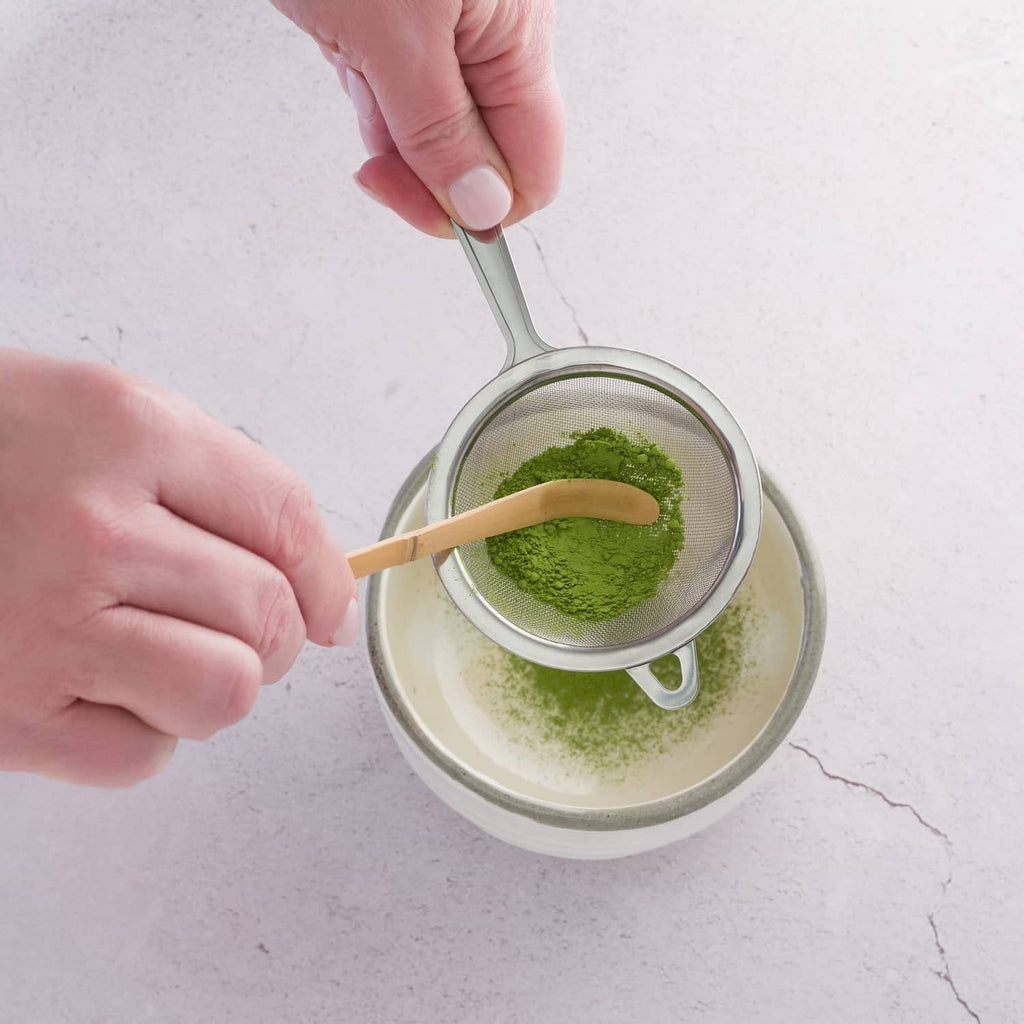 Stainless steel tea strainer sifting fine matcha powder into a bowl