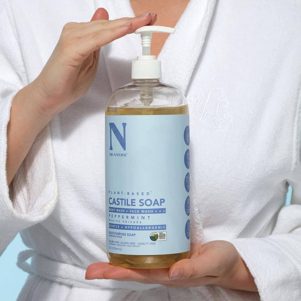 Castile soap bottle close-up held in hands, white pump dispenser and blue label.