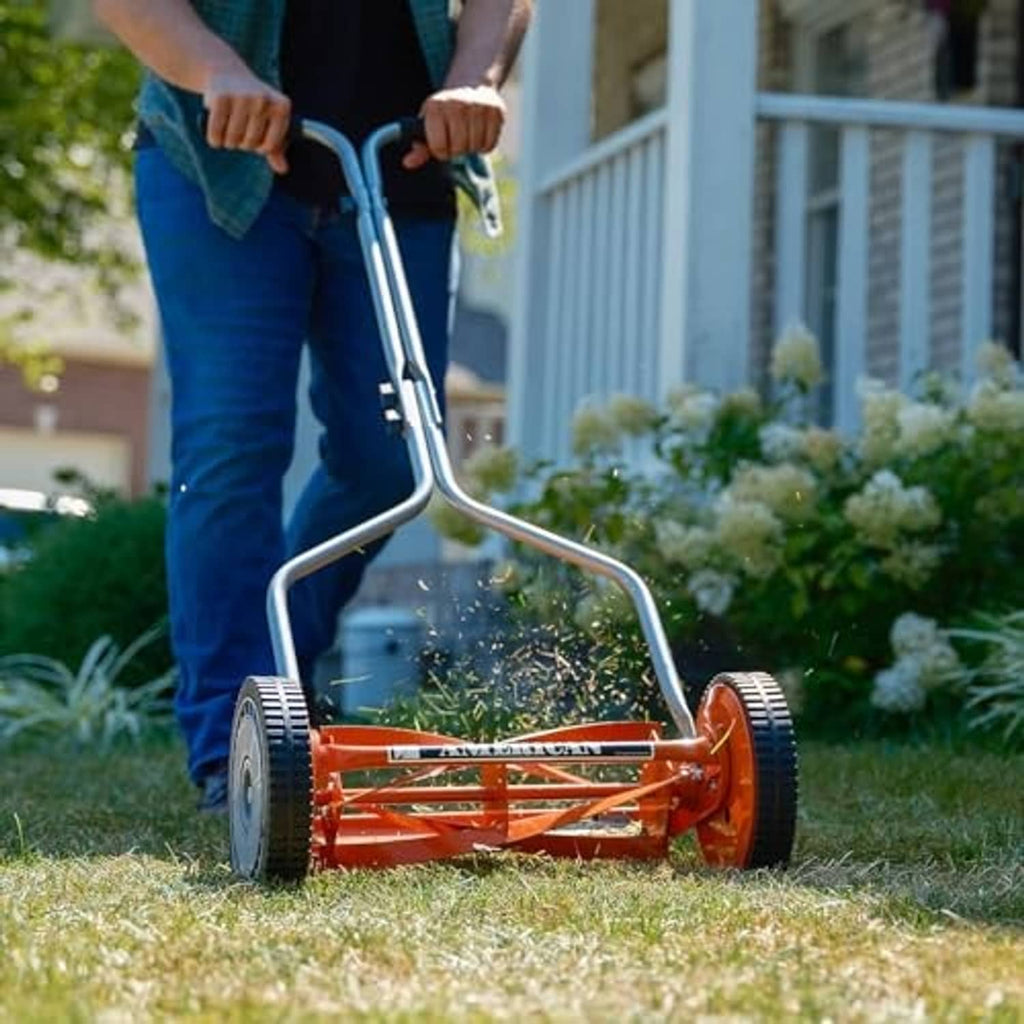 Red push reel lawn mower being pushed with silver handle and orange cutting deck