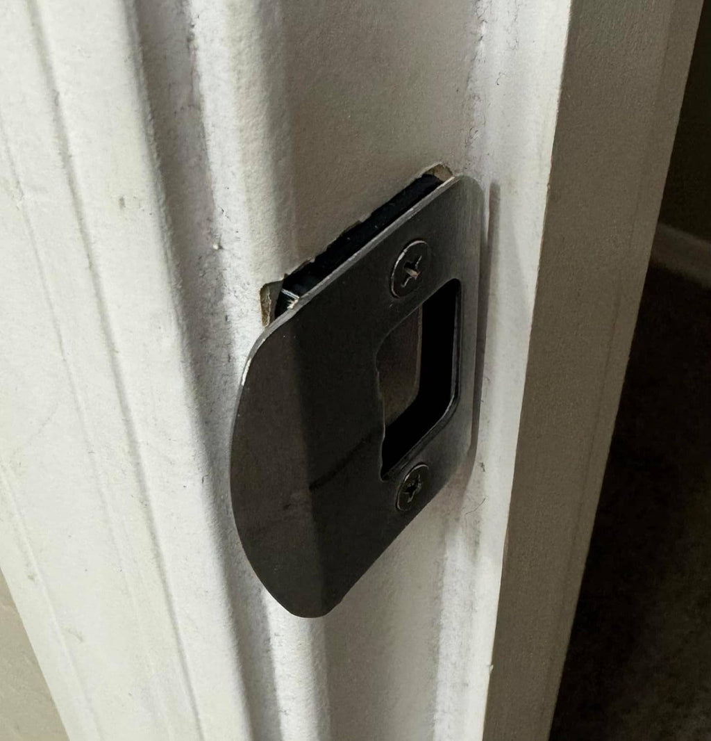 Black door strike shim spacer installed on a door frame strike plate