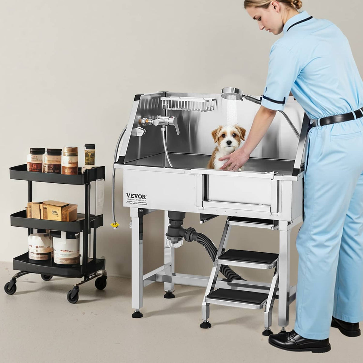 Pet groomer standing at stainless steel tub with front stairs and attached hose