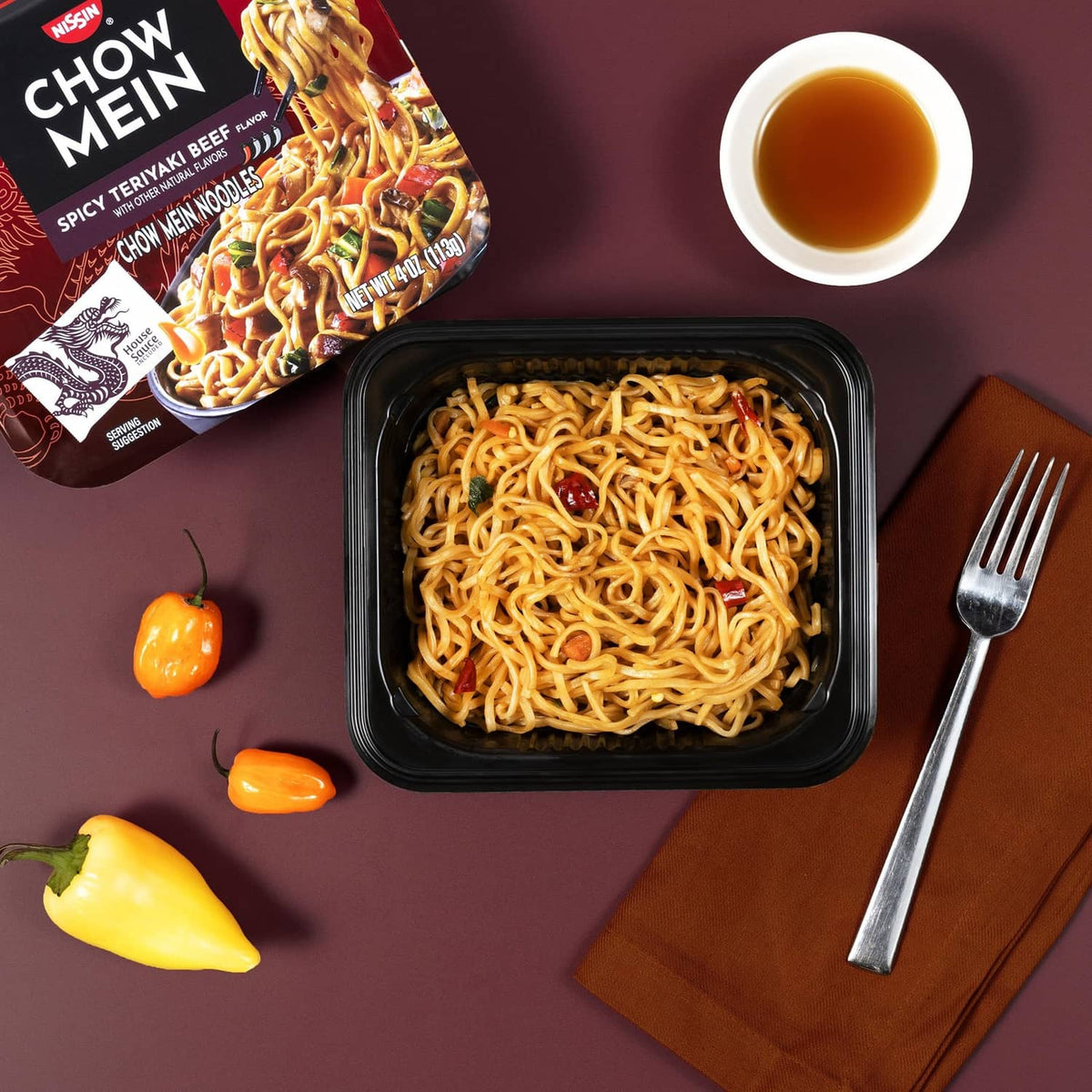 Chow mein noodles in black tray with sauce cup, chili peppers, and spicy teriyaki beef packet