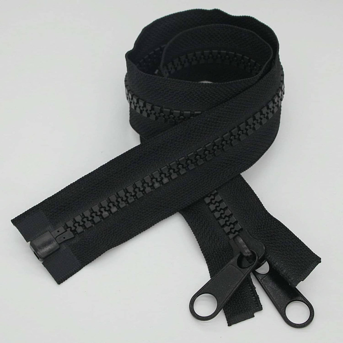 Black plastic separating zipper set with slider and two pull tabs, laid flat