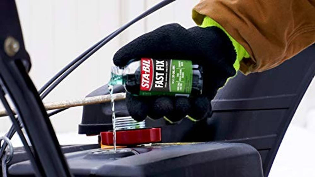 Person wearing gloves holding STA-BIL Fast Fix bottle above a vehicle battery
