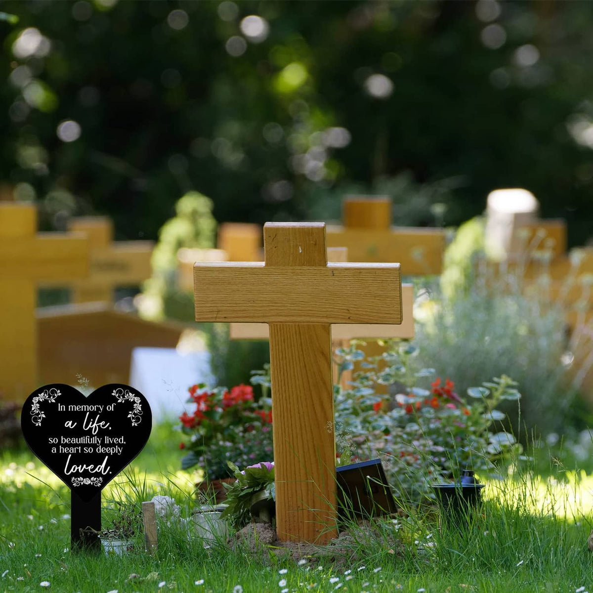 Heart-shaped black remembrance plaque with white verse on stake among garden graves.
