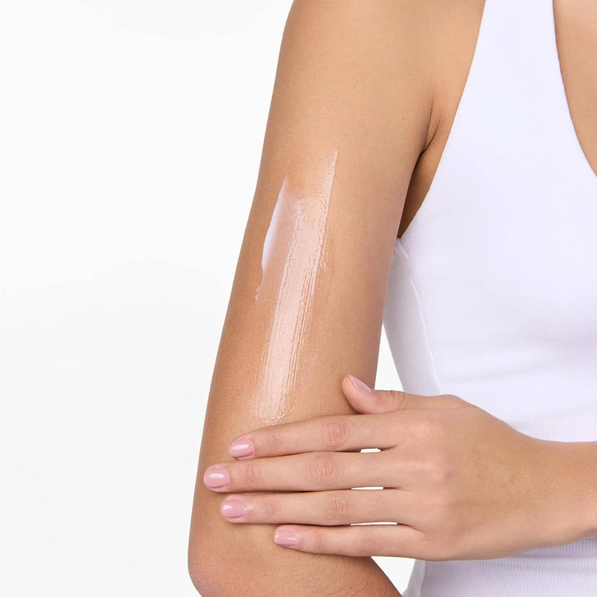 Close-up of applied glossy self-tan lotion on arm, smoothed by hand