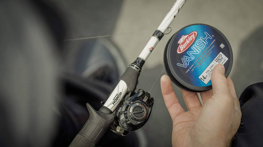 Clear fluorocarbon fishing line spool, 14 lb, held in hand near spinning reel.
