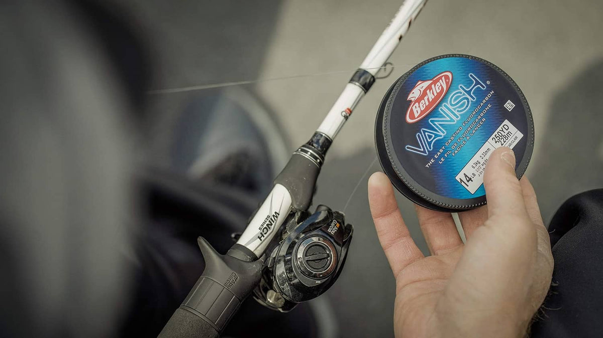 Clear fluorocarbon fishing line spool, 14 lb, held in hand near spinning reel.