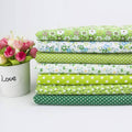 Bundle of folded cotton quilting fabrics with green, blue, and white patterns