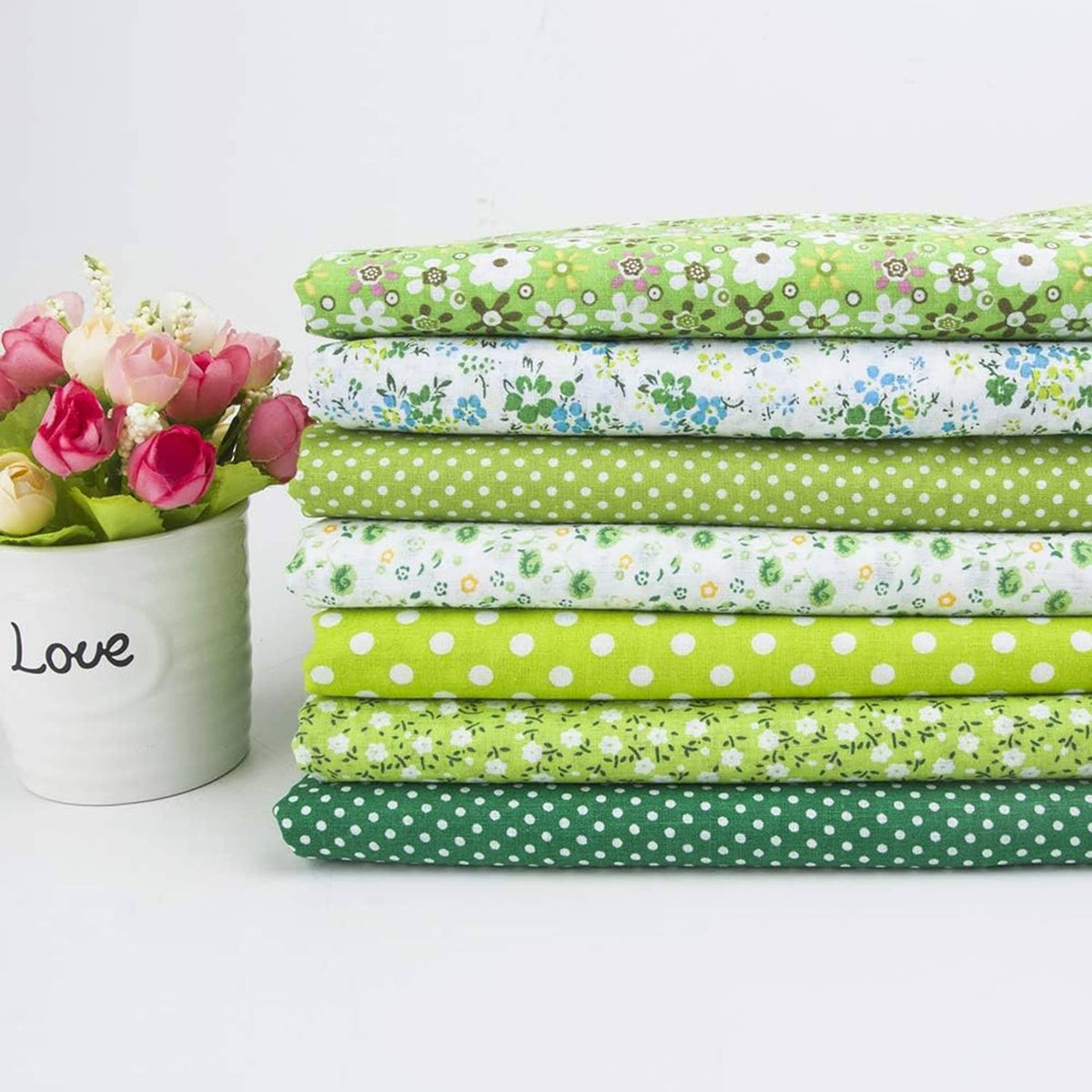 Bundle of folded cotton quilting fabrics with green, blue, and white patterns