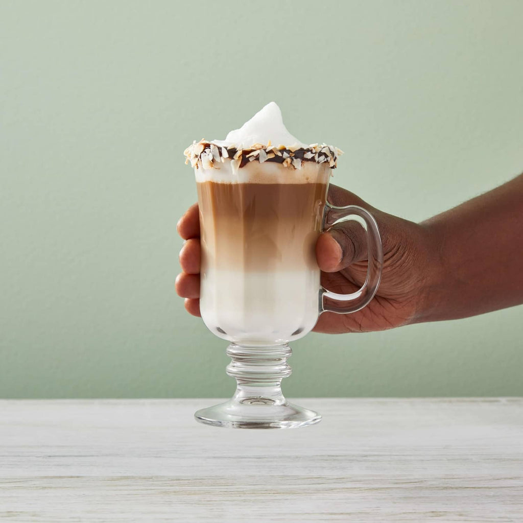 Hand holding a coconut syrup latte in a clear glass with whipped foam