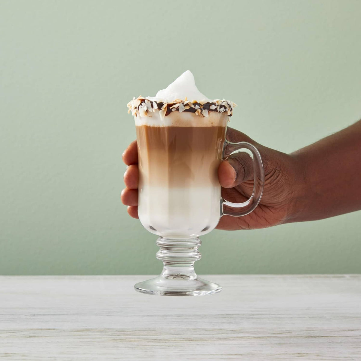 Hand holding a coconut syrup latte in a clear glass with whipped foam