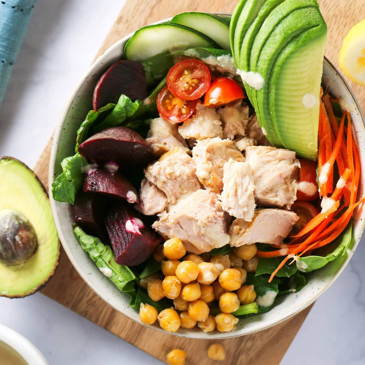 Albacore tuna salad bowl with tuna pieces, greens, avocado slices, tomatoes, carrots, chickpeas