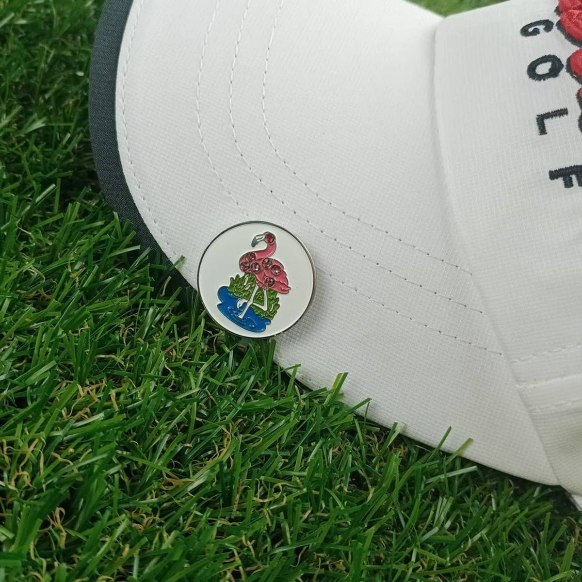 Flamingo golf ball marker clipped to white cap; round metal coin with pink flamingo art
