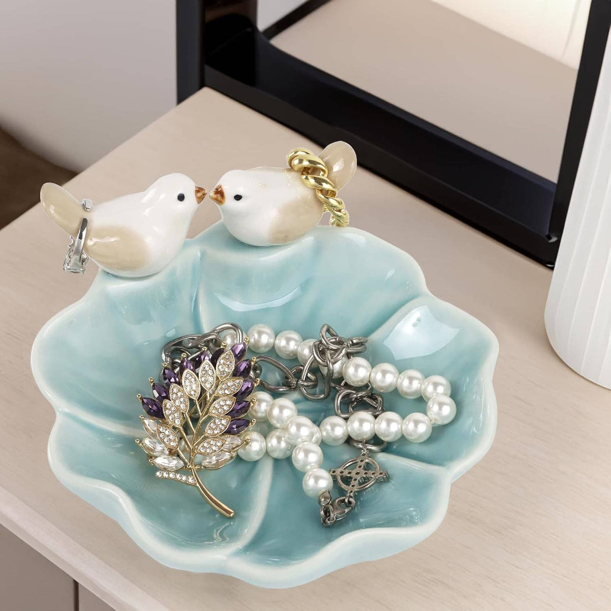 Ceramic lotus leaf jewelry tray with two white bird ring holders holding pearl necklaces and a purple brooch