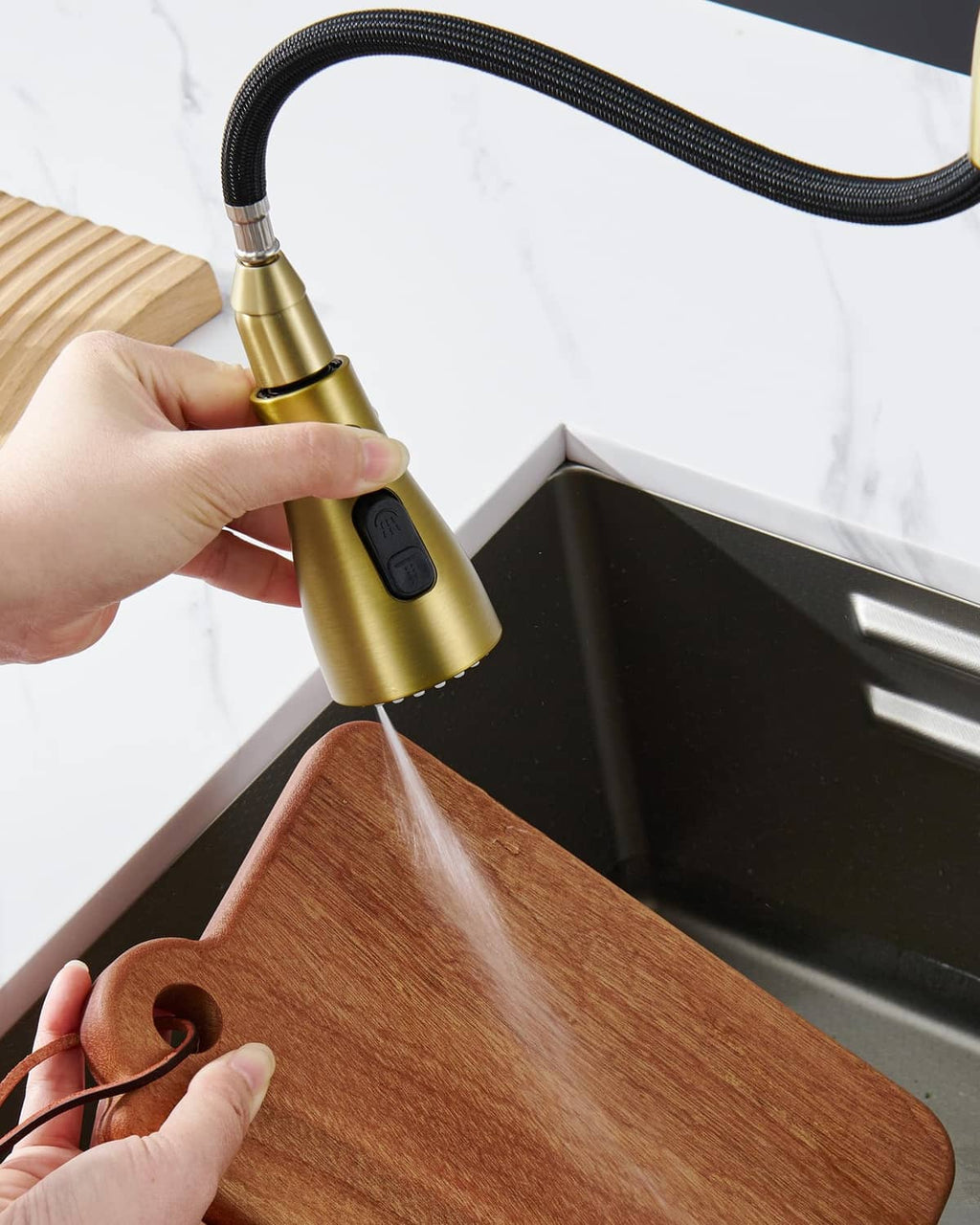 Brushed gold sprayer head releasing water onto a wooden cutting board