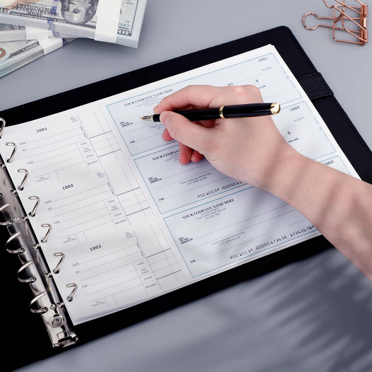 Black checkbook binder open to printed checks with hand writing on forms