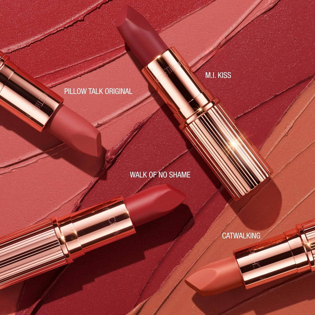 Multiple rose-pink matte lipsticks in rose-gold tubes on textured makeup palette