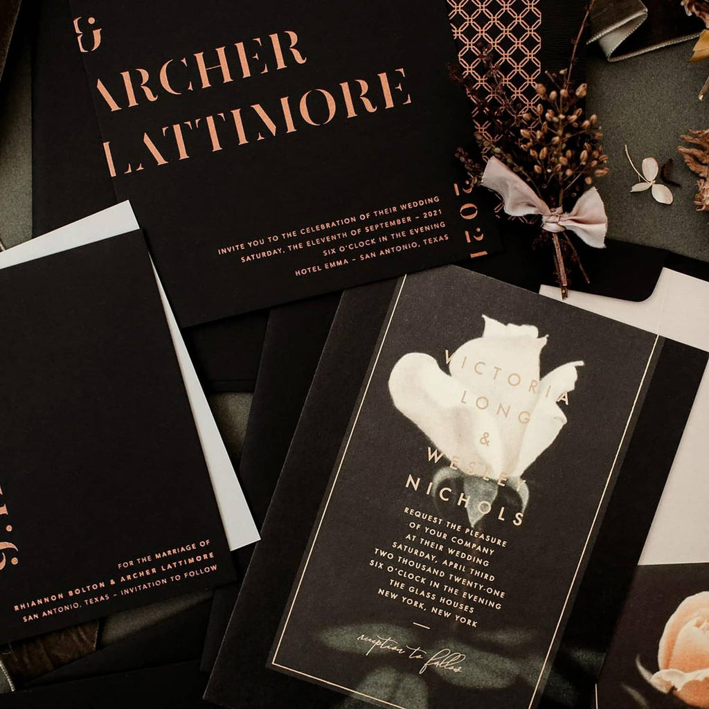 Black wedding invitation cards on a cardstock stack, with gold and white printed text.