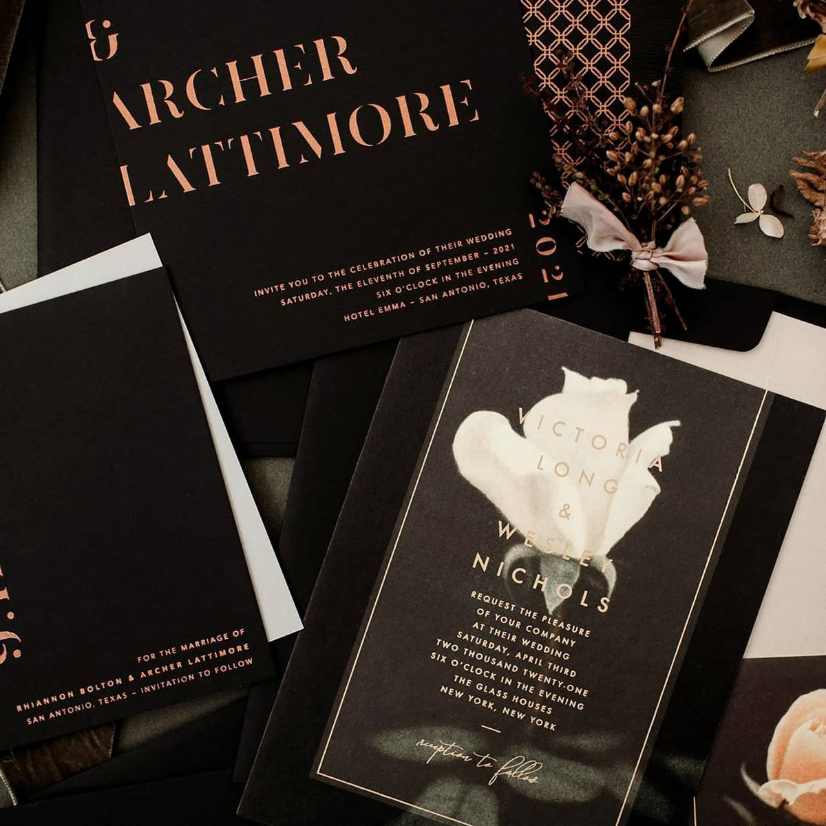 Black wedding invitation cards on a cardstock stack, with gold and white printed text.