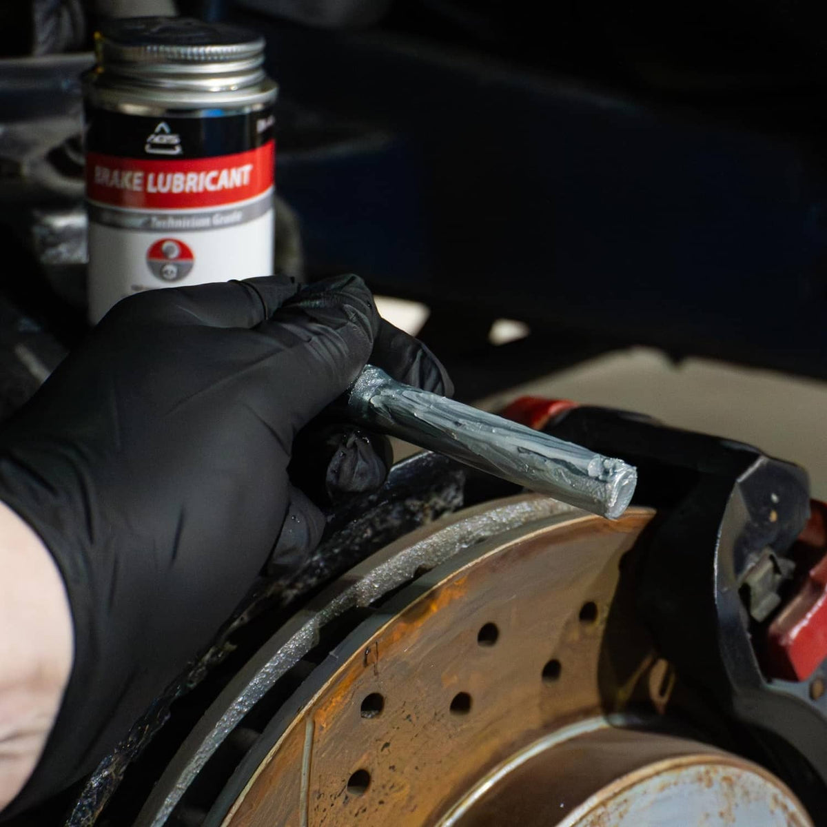 Gloved hand holds AGS SIL-Glyde silicone brake grease while brushing
